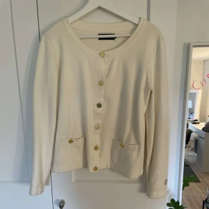 Vit kofta från Stockh LM med guldknappar - Säljer en stilren vit kofta från Stockh LM med rund halsringning och dekorativa guldknappar framtill. Koftan har två fickor fram och långa ärmar. Storlek M💗Använd inte köp nu!