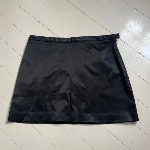 Svart satin-kjol från Zoul - Snygg svart kortkjol i satin från Zoul. Kjolen har en enkel och stilren design med lätt glansigt material och en liten slits framtill. Perfekt att matcha med en cool topp eller stickad tröja. Skriv för fler bilder💞