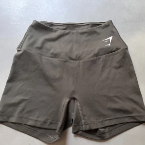 Olivgrön träningstights shorts från Gymshark - Olivgrön, tighta träningstights shorts från Gymshark med hög midja och diskret logga framtill. Perfekta för gymmet eller löpning. Väldigt mjukt! Kan köpas tillsammans med bh för 350kr 💕