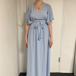 Balklänning - Säljer en ljusblå långklänning med v-ringning och korta vida ärmar från bubbleroom. Klänningen har ett knytband i midjan och ett litet sprund i ryggen. Perfekt till balen och enbart använd en gång!