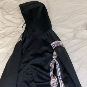 Burberry hoodie - Svart hoodie med dragkedja och huva. Har rutiga detaljer längs ärmarna och insidan av huvan. Aldrig använd. Kan gå ner i pris vid snabbaffär!!!!