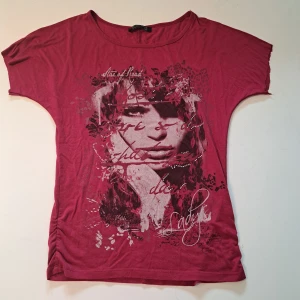 Mörkrosa t-shirt med tryck från Blind Date - Mörkrosa t-shirt från Blind Date med ett stort grafiskt tryck framtill i svart och vitt. T-shirten har rund halsringning och korta ärmar. Ärmarna är avklippta men det är inget som syns när den bärs.