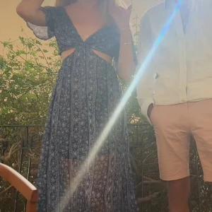 Blå långklänning med blommigt mönster från Pepe Jeans - Säljer en blå långklänning från Pepe Jeans med blommigt mönster och v-ringning. Klänningen har korta ärmar, cut-out detaljer vid midjan och ett luftigt, flowy tyg. Perfekt för sommaren!