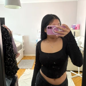 Svart långärmad topp från Gina Tricot - Säljer en svart långärmad topp från Gina Tricot med fyrkantig urringning och ribbad struktur. Toppen har en figurnära passform och är croppad, vilket ger en trendig look. Perfekt att styla med höga jeans eller kjol.