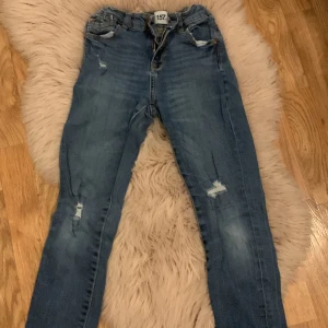 Blåa Jeans  - Vanliga jeans med hål i knäet . Storlek 140