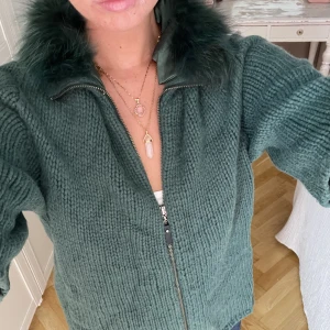 Kashmir zip up - En underbar smaragdgrön kortärmad kashmirkofta med äkta tvättbjörnspäls från Steffen Schraut. Oanvänd.