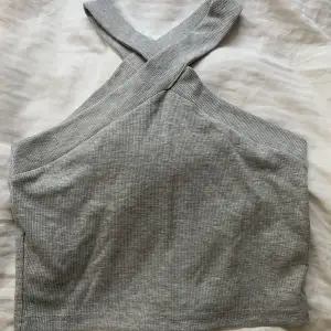 Ett grått linne med korsade armar runt nacken. Köpte i trepack men behöver inte tre så inte använd! 
