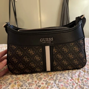 Guess axelremsväska  - Äkta guess axelremsväska i nyskick, Mått: Längd:26cm Bredd:8cm Djup:14cm