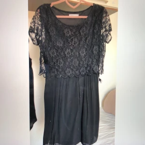 Klänning  - Svart fin festklänning med spetsdetalj upptill. Längd ca 95 cm. Kort spetsärm. Som ny. L men passar säkert även M.