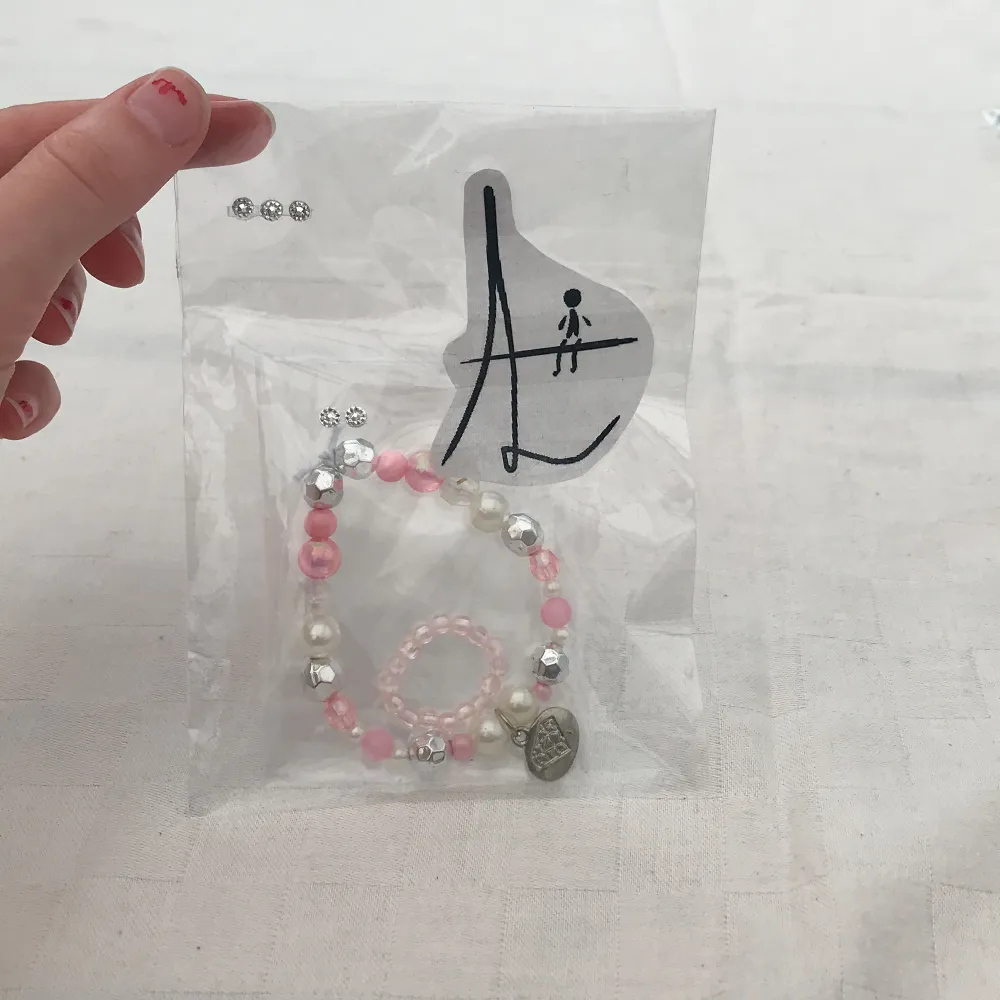Hemmagjord ring och armband med vit elastisk tråd. Ett litet hänge på med en diamant och ordet ”elements”.. Accessoarer.