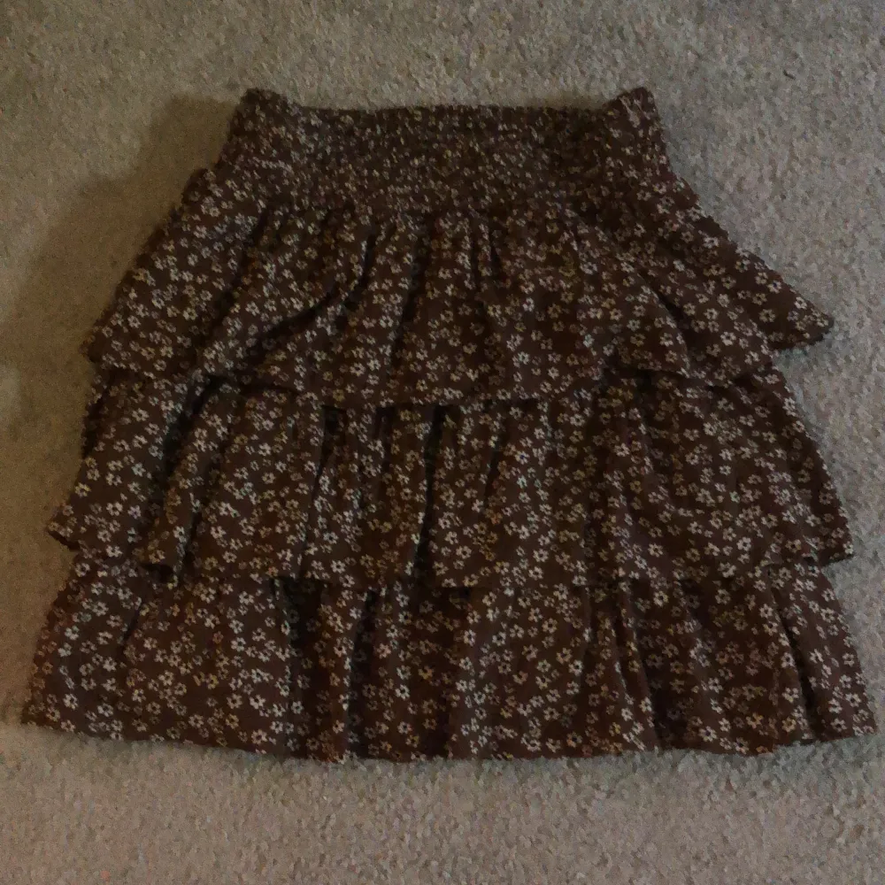 En brun blommig kjol från Lindex i storlek 158-164. Det är en liten fläck på sidan som knappt syns. En liten del av tråden på en av volangerna är borta men sytt igen så den inte går upp ännu mer.Säljer den för den inte kommer till användning längre.😍. Kjolar.