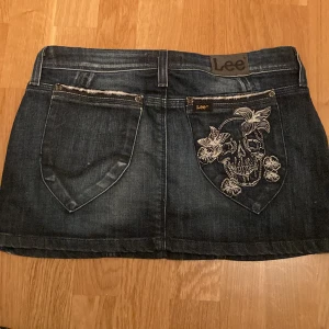 Jeanskjol med tryck  - As cool jeanskjol med döskalle tryck på fickan. Köpt secondhand i Spanien. Midjemått: 76cm Höftmått: 88cm Längd: 28cm