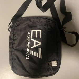Armani axelväska - Jag köpte den här armani väskan för 599kr och jag har aldrig använt den så den är i perfekt skick, jag säljer den eftersom det inte är min stil. Den passar för både tjejer och killar 