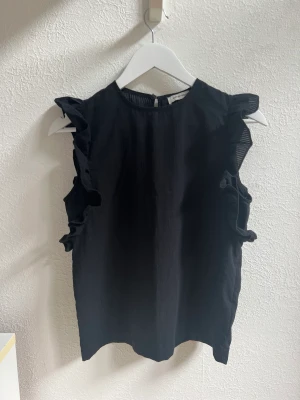 Svart blus med volanger  - Svart blus med volanger på ärmarna. Från Åhléns och märket Carin Wester. Storlek Xs, bra skick!