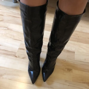 Höga stövletter - Klackar som slutar precis under knäna på mig som är 174 cm lång, dom är glansiga och har ormskinnsmönster. Endast använda en kväll så dom är nästan som nya. Klackhöjden är 8 cm och omkretsen runt låret är ca 42/43 cm