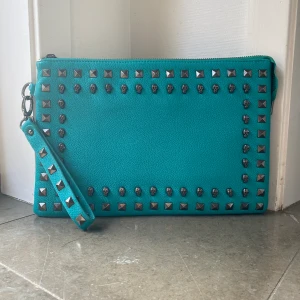 Datorväska med nitar - Säljer denna fina datorväska eller clutch som jag precis fått hem från Sellpy med nitar och dödskallar då den var för liten för min dator! Liten slitning vid handtaget, kontakta mig för fler frågor, köpare står för frakt, KLICKA GÄRNA PÅ KÖP NU!