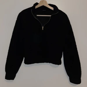 Croppad Teddy tröja, stl.XS. - En svart Croppad Teddy tröja med dragkedja vid halsen från Gina Tricot, stl. XS.  I använt skick, men inga som helst defekter.
