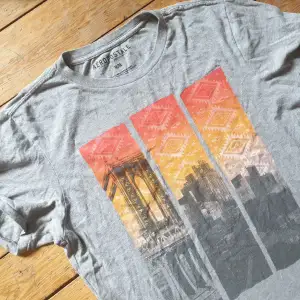T-shirt i grått med tryck av Brooklyn(?). Bohemisk mönster design i bakgrunden 