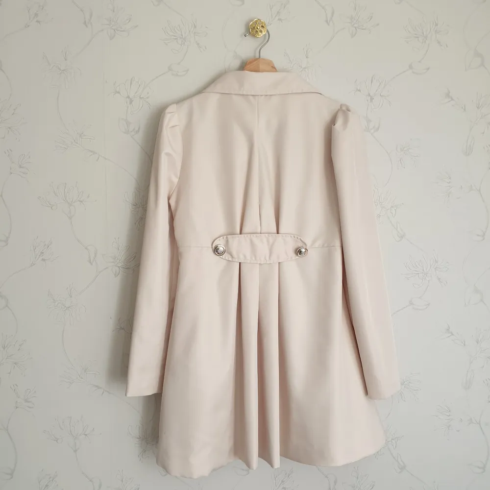 🩷FÖRST TILL KVARN!🩷 Super söt beige trenchcoat med guldfärgade knappar. Kappan har puffärmar och volanger i baksidan, fockor i fram. Dock finns en fläck i fram (tredje bild) som jag inte lyckats få bort, därav priset. Vill bli av med ASAP!. Jackor.