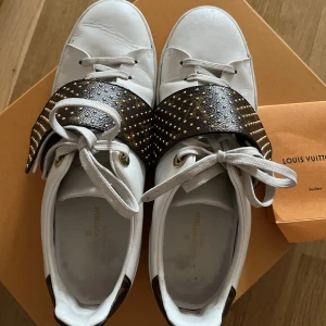 Loui Vuitton sneakers  - Vita Loui Vuitton sneakers med en brun monogram kardborreband med guldiga nitar på.  Storlek 39  Köpta i Milano 2019, dustbag till skorna kommer med även nya skosnören samt kvitto! 