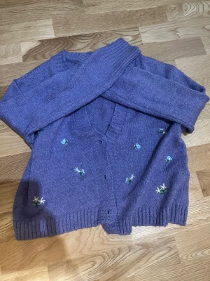 Broderad kofta - Lila stickad kofta med broderade detaljer. Saknar dock knappar och pris kan därför diskuteras.
