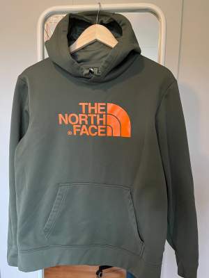 Mörkgrön The North Face hoodie med orange text, storlek M 
