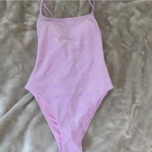 Glittrig baddräkt - Super söt glittrig, rosa baddräkt från H&M med öppen rygg. Aldrig använd, har alla lappar kvar och köpt för 300kr frakt tillkommer 💕