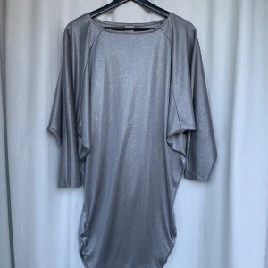 Silverklänning från Ginatricot - En helt oanvänd silverklänning från Ginatricot, strl S. Vida ärmar, oversized överdel. Avslutas med rynk som sitter snyggt på låret.