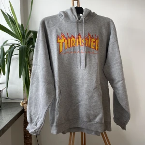 Thrasher hoodie L - Grå hoodie från Thrasher, unisex. Storlek L.   Använt men fint skick, det enda jag hittar att anmärka på är en liten tråd i ena snöret som gått upp (se bild). Ej nopprig i tyget, möjligen lite ”sträv” jämfört med nyskick som hoodies lätt blir efter tvätt.