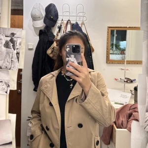 Beige kappa  - Tillkommer även en luva och ett band som är avtagbart.  