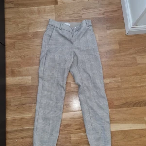 Slacks/ kostybbyxor från hm - Ett par ankellånga slacks i stretchig, vävd kvalitet. Byxorna har dold resår i midjan och avsmalnande ben. Sidfickor samt fuskfickor bak. Normalhög midja. Gylf med dragkedja samt dold hyska och hake.  Artikelnummer:0751471097 Längd: Ankellång Midjehöjd: N