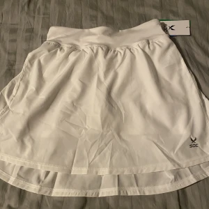Soc padel/tennis kjol - Vit padel/tennis kjol, från märket soc. Strolek 158-164, finns snöre och under short med bollficka. Helt nya med lapp kvar säljer på grund av att jag har en likadan redan sen innan. Nypris 299 kr