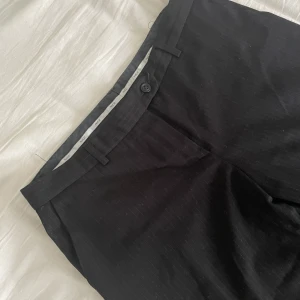 Kostymbyxor - Svarta lågmidjade kostymbyxor med smala vita ränder, dom e raka i benen o ganska vida