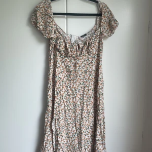 Blommig klänning - Blommig vit klänning med grönt och beige/rosa. Strl L, lite stor på mig därav att jag säljer. Endast använd 1 gång. Liten slits och dragkedja vid ryggen. Sitter jättefint på! 