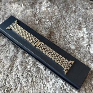 Armband till Apple Watch - Säljer ett silvrigt armband med ”diamant” detaljer till Apple Watch.  Armbandet passar storlek 42/44/45. Armbandet är aldrig använt, så nytt. Finns även två extra länkar så att man kan justera längden.