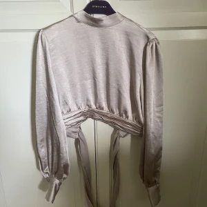 Satinblus med öppenrygg - Champagne färgad satinblus med öppen rygg i något croppad modell 