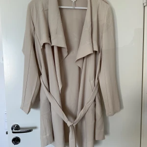 Kort Kappa - Den här kappan är köpt från Ellos ord.pris 499kr. Storlek S och färgen Sandshell, på bilden är den mer beige men den är gul. Jag har använt kappan en gång så jag anser den som ny!