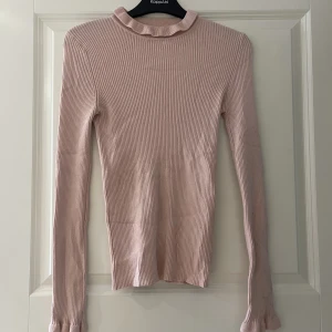 Tröja  - Gammelrosa tröja som har något polokrage och sitter slimat på kroppen utan att vara tajt. I mycket gott skick. Har volanger i både krage och ärmslut