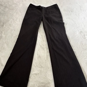 Lågmidjade bruna kostymbyxor - Säljer ett par Lågmidjade kostymbyxor från VILA🤎  De är randiga med väldigt smala ränder, breda nertill och långa i benen, väldigt bra skick!  Storlek-M men skulle säga att de är lite mer som S