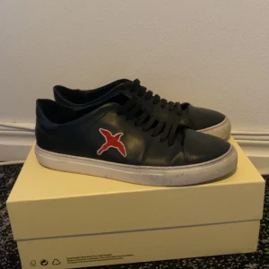 Axel Arigato clean 90 red bird  - Axel Arigato clean 90 red bird. I använt skick, hälen på den högra skon är lite sliten, nån repa vid tån men inget stort. Finns inte och köpa på hemsidan längre. Box ingår. Nypris 2500kr
