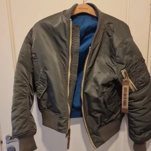 Alpha bombarjacka - Grön bombarjacka från alpha, en lite smalare modell än den med orange foder. Storlek medium, 4 fickor och den klassiska cigarett fickan. Vändbar. Blått foder med en patch på ena ärmen