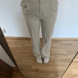 Högmidjade beiga kostymbyxor  - Raka ben, med pressveck. Högmidjade ljus beige färg. Mycket bra skick
