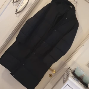 Lång vinterkappa - Lång, svart vinterkappa med luva, knappar och dragkedja. Everest/Stadium storlek 42. 