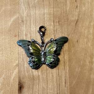 Ett fint hänge med en fjäril i grön färgskala, kan användas på både halsband och nyckelring