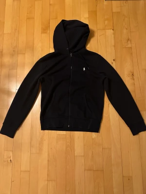 Mörkblå Ralph Lauren ziphoodie i storlek S - Oanvänd ziphoodie som passar om man är 177-181 cm lång. Säljer en annan med samma modell, och om man köper båda så tar jag 2000 för båda.