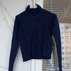 Stickad tröja  - Blå stickad tröja, med knappar i kragen och små rutor på framsidan 