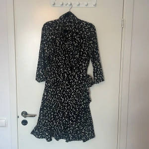 Klänning VERO MODA - Svart mönstrad klänning med krage och knyt i sidan.