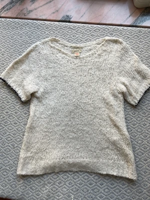 Kortärmad stickad tröja - Kortärmad stickad tröja som är lite fluffiga, ifrån Bellerose. Tröjan är krämvit och har en mörkblå kant runt ärmen. Den är ifrån barnavdelningen i storlek 10 men passar mig som har XS. 