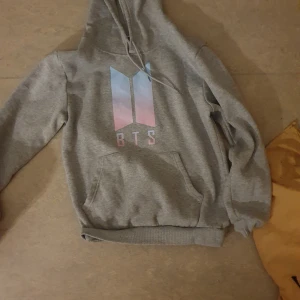 BTS HODDIE - En grå hoddie för alla armies där ute! Den är sjukt mjuk och skön på insidan köpte från Amazon drygt 2 år sen! På baksidan är den små bilder av alla o bandet och deras namn!