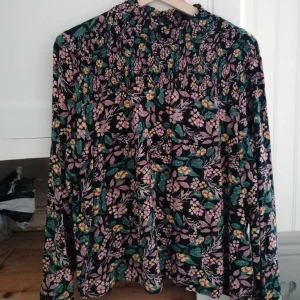 Blommig polo tröja - En blommig polo med ballongärmar, knappar bak i halsen och "resår" på bröstet. Storlek XL men jag som är S har använt som oversize. Väldigt skönt material